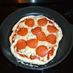 A skillet filled with a pizza crust topped with cheese and pepperoni.