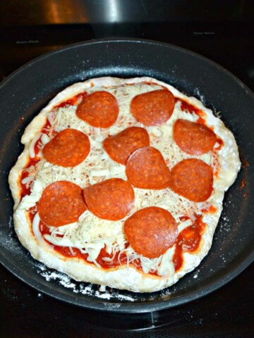A skillet filled with a pizza crust topped with cheese and pepperoni.