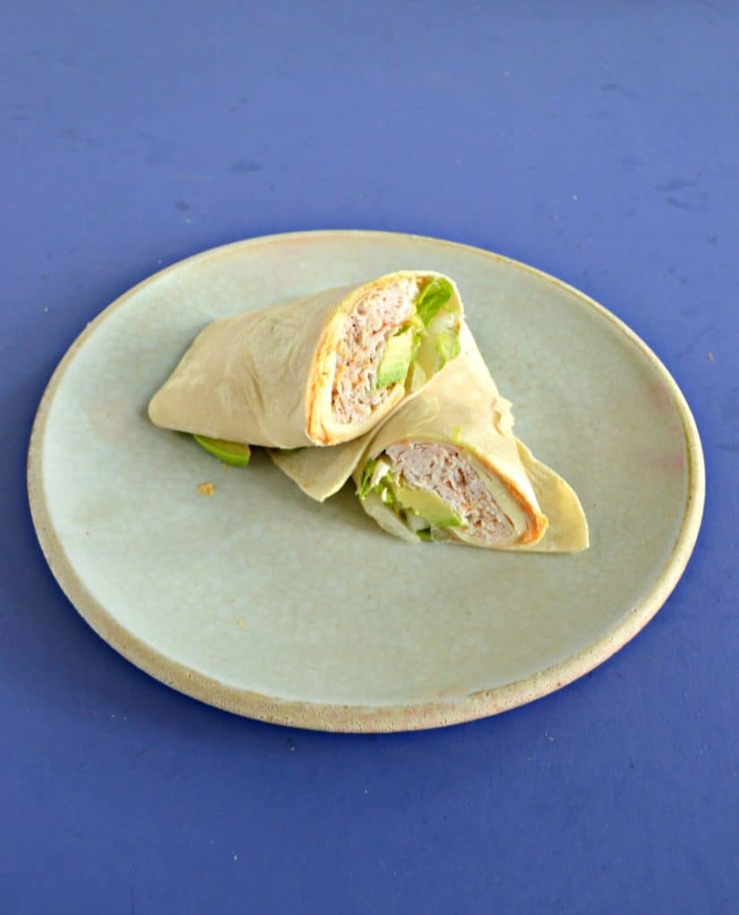 A plate with a turkey wrap on it, cut in half, and stacked on top of each other.