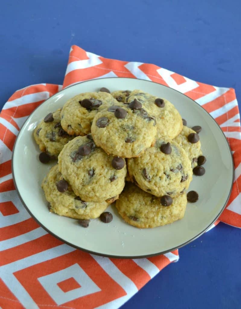A plate piled high with chocolate chip cookies set on an orange napkin.