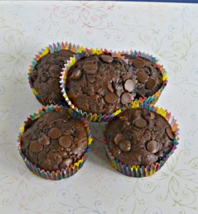 Four chocolate chip muffins on a white background with one muffin sitting on top of the pile.