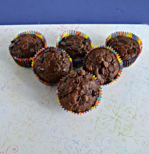 Three rows of chocolate muffins. Three muffins in the back, two in the middle, and one in the front tilted toward the camera on a white background.