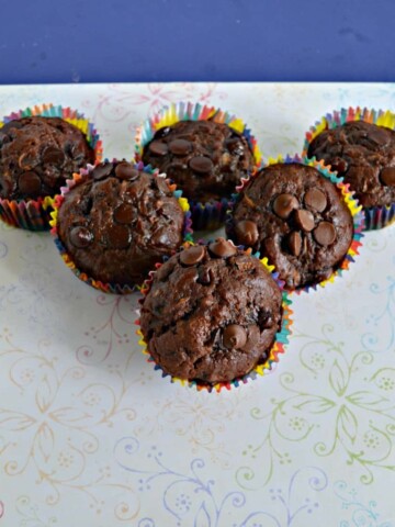 Three rows of chocolate muffins. Three muffins in the back, two in the middle, and one in the front tilted toward the camera on a white background.