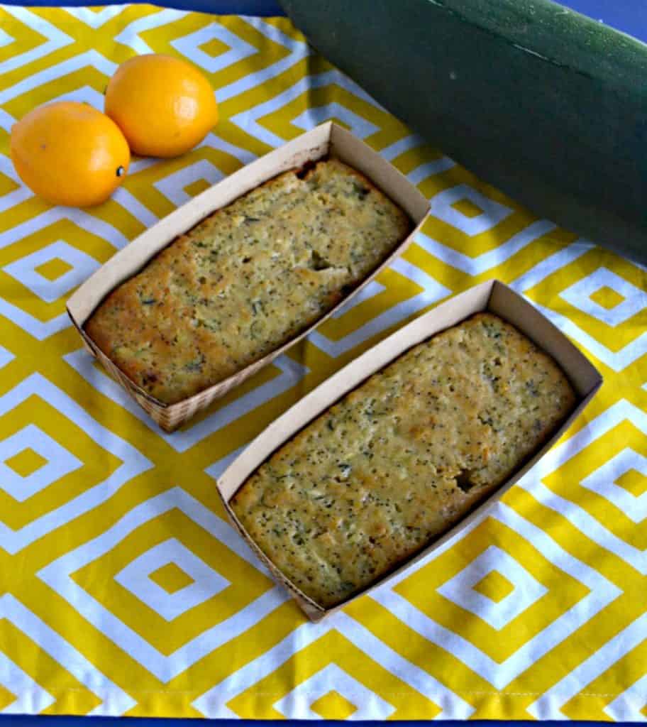 A yellow and white placemat with two mini loaves of bread sitting diagnal with two yellow lemons in one corner and a green zucchini in the other corner.