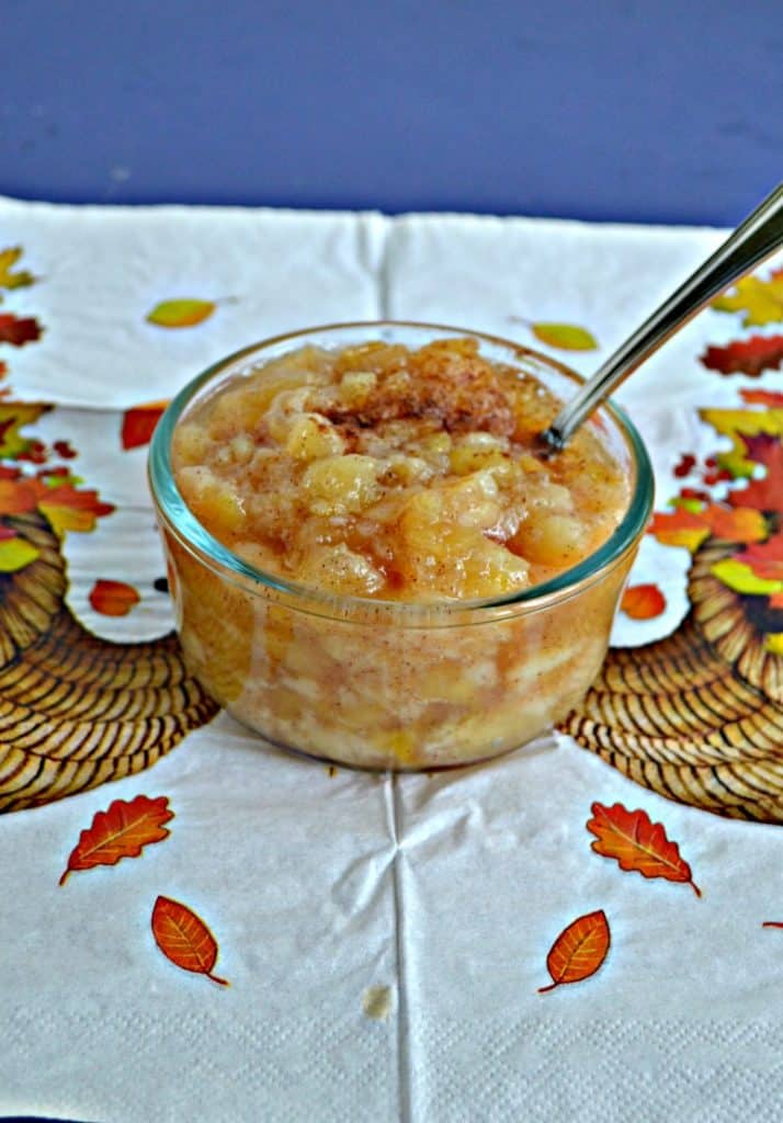 Close up of a bowl of pear and apple sauce with a spoon sticking out of it on a background of cornucopias and fall leaves.