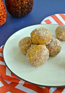 A close up of three donut holes with one donut hole balancing on top sitting on an orange and white napkin.