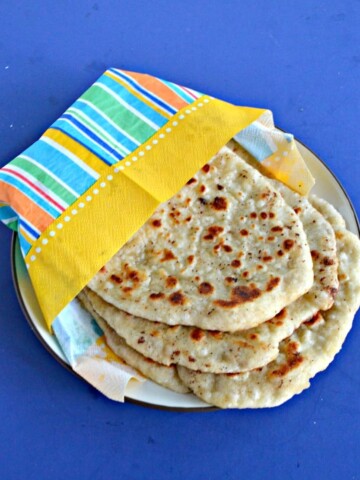 A plate with three Naan flatbread wrapped in an orange, blue, and yellow napkin on a blue background.