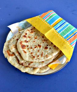 A plate with a stack of Naan wrapped in an orange, yellow, blue, and green napkin on a blue background.