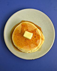 A plate piled with a stack of 3 pancakes on a blue background.