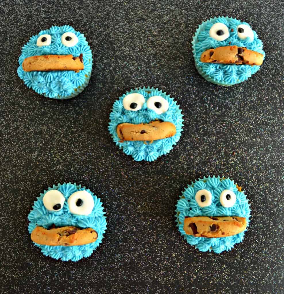 Five cupcakes arranged in an X, each one topped with blue frosting, google candy eyes, and a half cookie mouth that looks like Cookie Monster.
