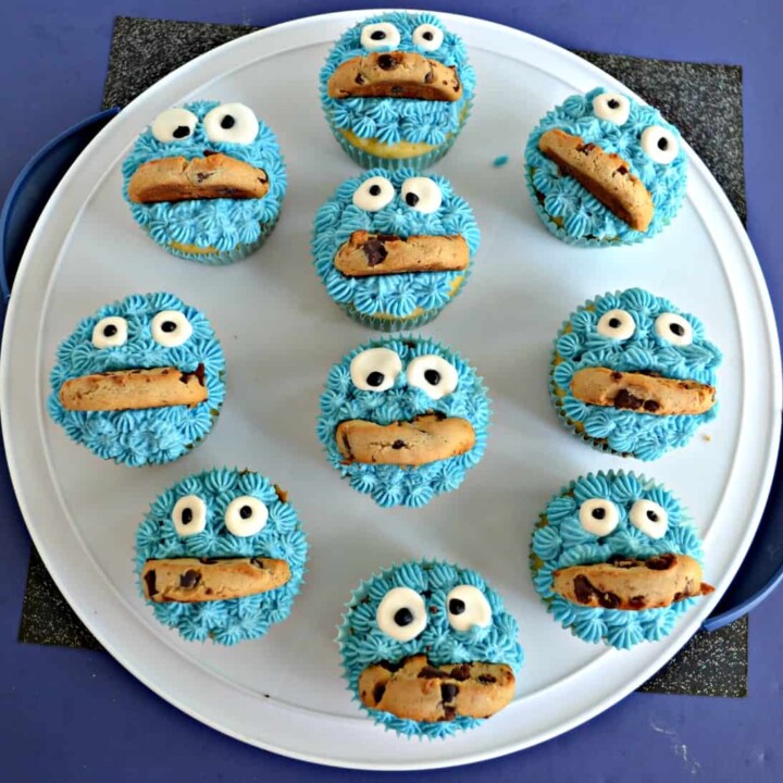 A large white platter scattered with cupcakes decorated like Cookie Monster with blue frosting, google candy eyes, and half a cookie mouth.