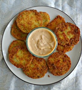 A plate topped with golden brown fried green tomatoes with a bowl of remoulade in the middle on a white background.