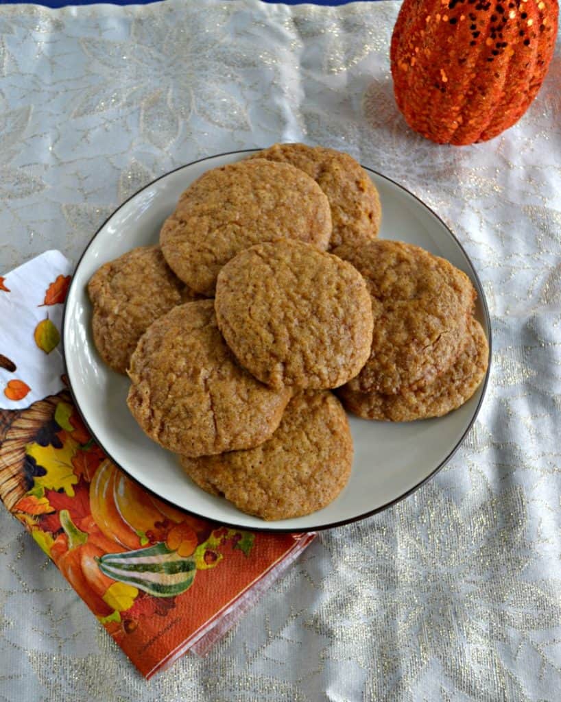 A white plate piled high with snickerdoodle cookies on top of an orange napkin with leaves on it and part of a pumpkin peeking in from the upper right hand corner. 