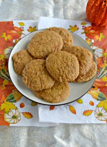 A long white, orange, and yellow napkin with leaves on it topped by a white plate piled high with pumpkin cookies.