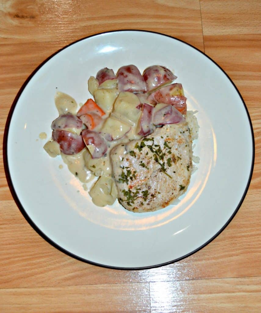 A white plate with a single browned pork chop on it along with red skinned potatoes and carrots in a white gravy.