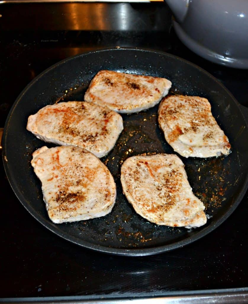 A black skillet with five browned boneless pork chops in it.