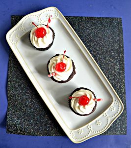 A top view of a white platter with three chocolate cupcakes on it with white frosting and a cherry on top on a sparkly black background.