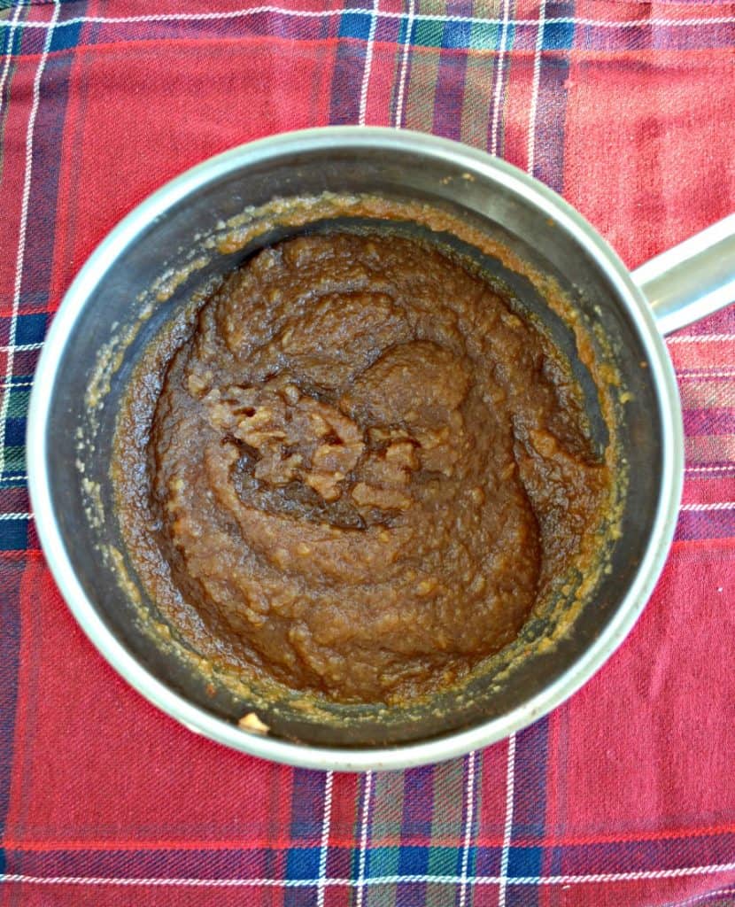 A pot filled with brown apple butter sitting on a red plaid background