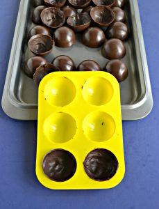 A baking sheet filled with chocolate spheres with a yellow silocone mold sitting upright on it with two circles filled with chocolate.
