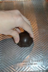 A hand pressing a half chocolate sphere onto a hot silver baking sheet.