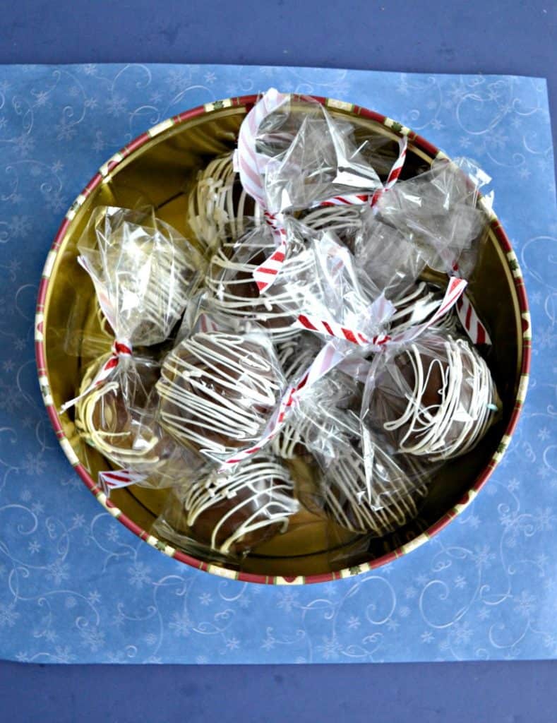 A tin filled with wrapped chocolate spheres tied with red and white ribbon on a blue background.