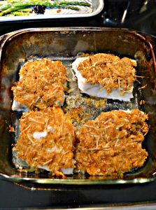 A baking dish with four fish filets with golden brown topping on each.