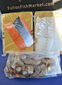 A vaccum sealed package of salmon filets, a vacuum sealed package of haddock filets, and a bag with huge shrimp in it.