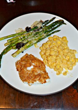 A white dinner plate with green asparagus in the upper left corner, yellow macaroni and cheese on the right side, and a piece of golden brown fish in the bottom left.
