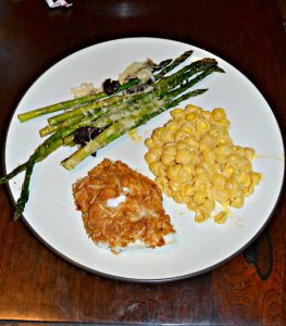 A white dinner plate with green asparagus in the upper left corner, yellow macaroni and cheese on the right side, and a piece of golden brown fish in the bottom left.