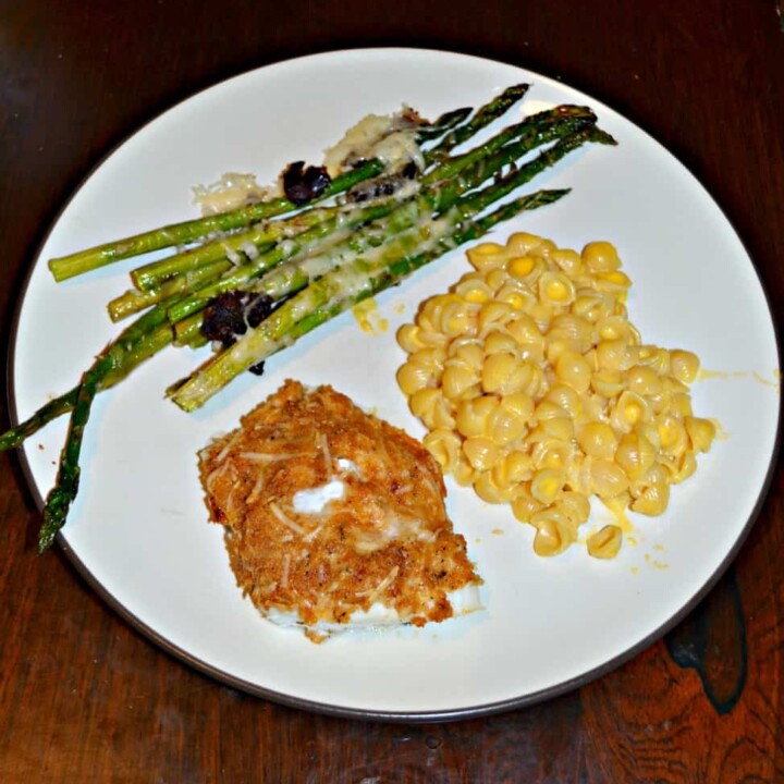 A white dinner plate with green asparagus in the upper left corner, yellow macaroni and cheese on the right side, and a piece of golden brown fish in the bottom left.