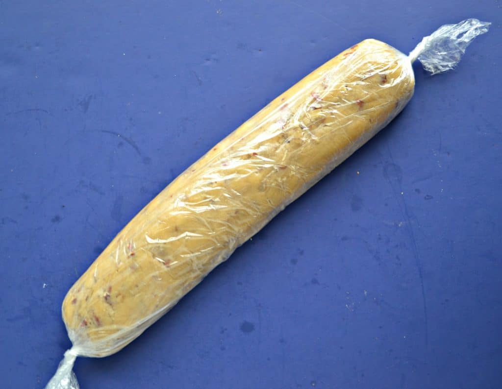 Cookie dough rolled in plastic wrap then twisted at the ends on a blue background.