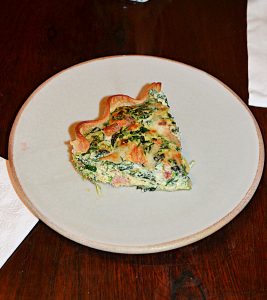A plate with a slice of Spinach and bacon quiche on it.