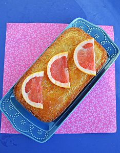 A loaf of grapefruit cake on a blue platter with three grapefruit slices on top.