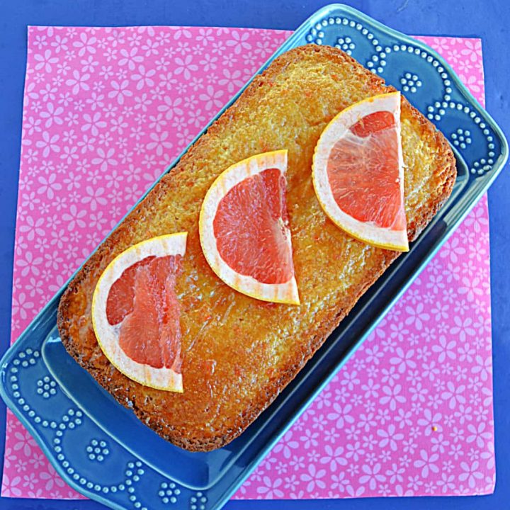 A loaf of grapefruit cake on a blue platter with three grapefruit slices on top.
