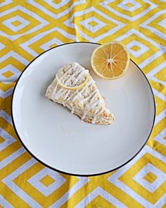 A large Meyer Lemon Scone on a white plate with a slice of lemon on a yellow and white background.