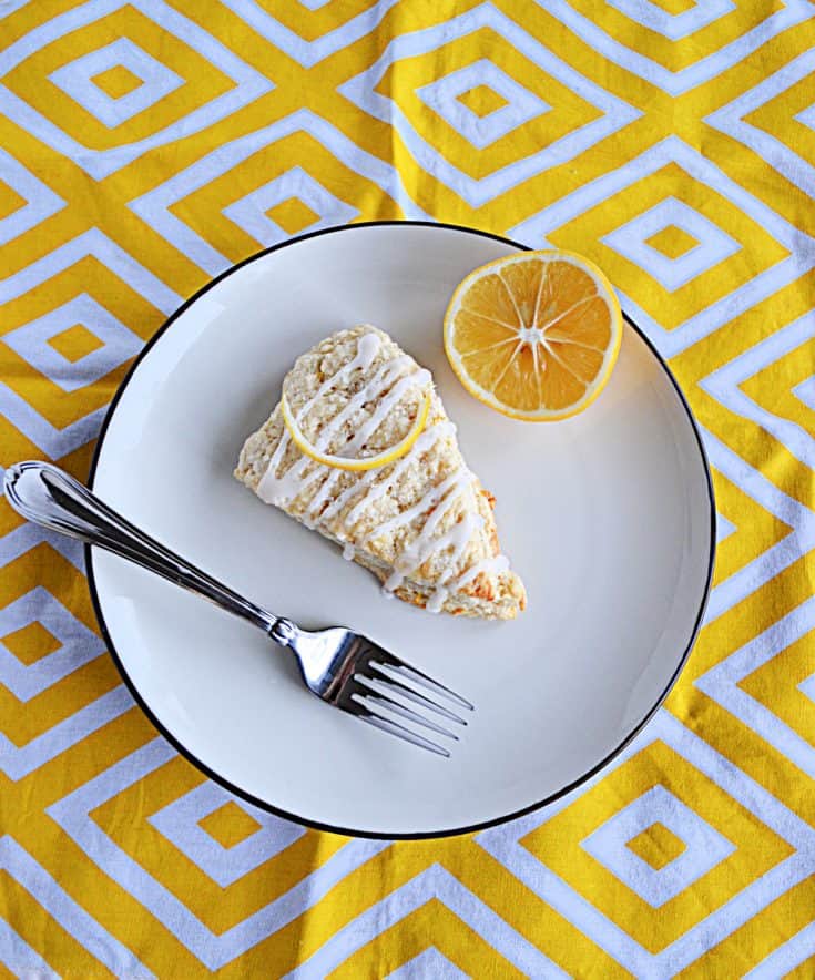 A large Meyer Lemon Scone on a white plate with a slice of lemon and a fork on the plate.