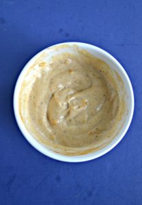 A white bowl filled with light orange remoulade sauce on a blue background.