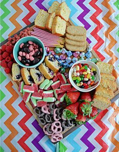 A colorful pastel dessert board filled with candies, cookies, fruits, and quick breads in Easter colors.