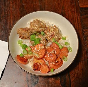 A bowl filled with rice, Firecracker meatballs, roasted carrots, and scallions.