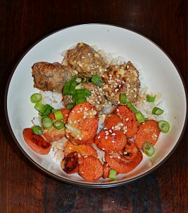 A close up of a bowl filled with rice, Firecracker meatballs, roasted carrots, and scallions.