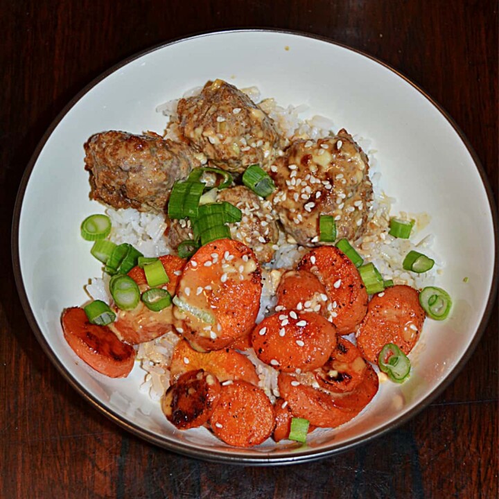 A close up of a bowl filled with rice, Firecracker meatballs, roasted carrots, and scallions.