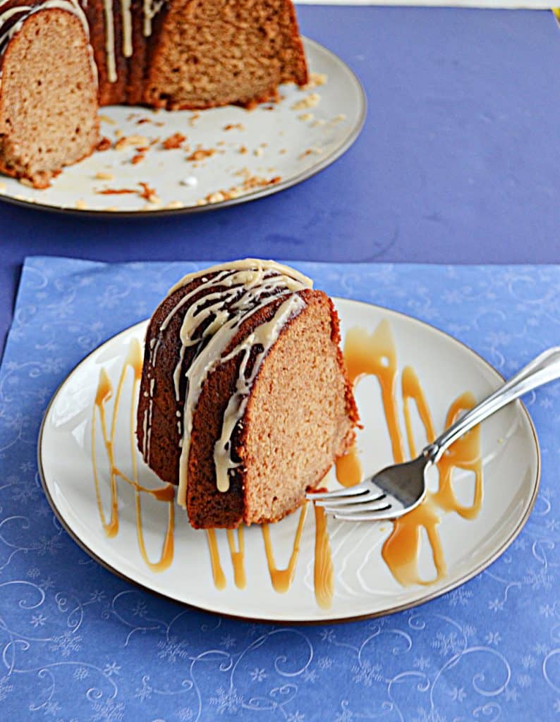 A close up of a plate with a slice of golden brown Bundt Cake topped with a glaze and the plate splatter with a caramel drizzle and the cut Bundt cake peeking in from the back left corner. 