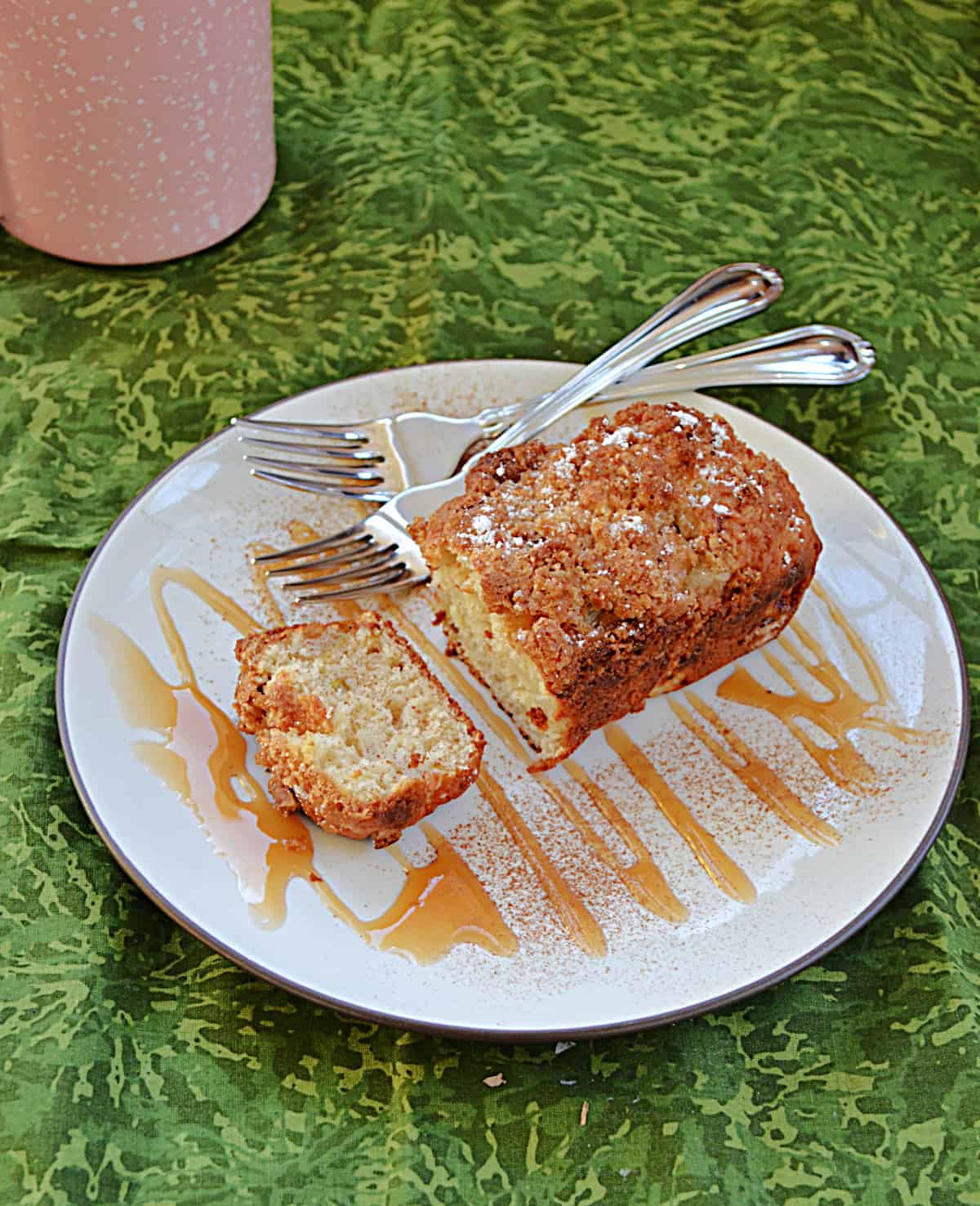 A plate drizzled in caramel sauce topped with a pear ginger mini cake with two forks on the plate and a coffee cup in the background.