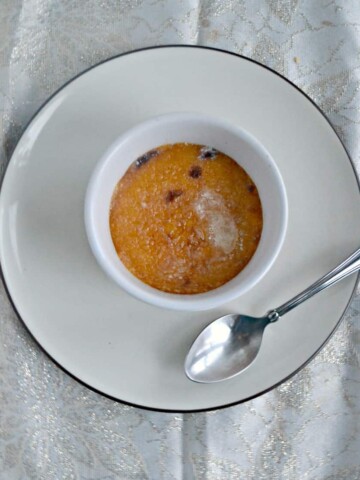 A ramekin of persimmon and cranberry creme brulee with a glass sugar top on a white dish with a serving spoon on the plate next to it.