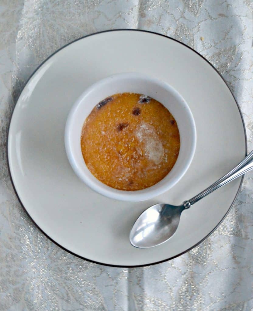 A ramekin of persimmon and cranberry creme brulee with a glass sugar top on a white dish with a serving spoon on the plate next to it. 