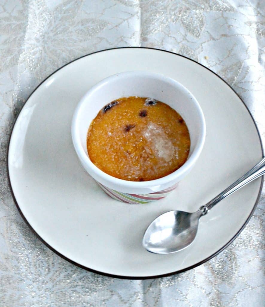 Front view of a ramekin of persimmon and cranberry creme brulee with a glass sugar top on a white dish with a serving spoon on the plate next to it. 