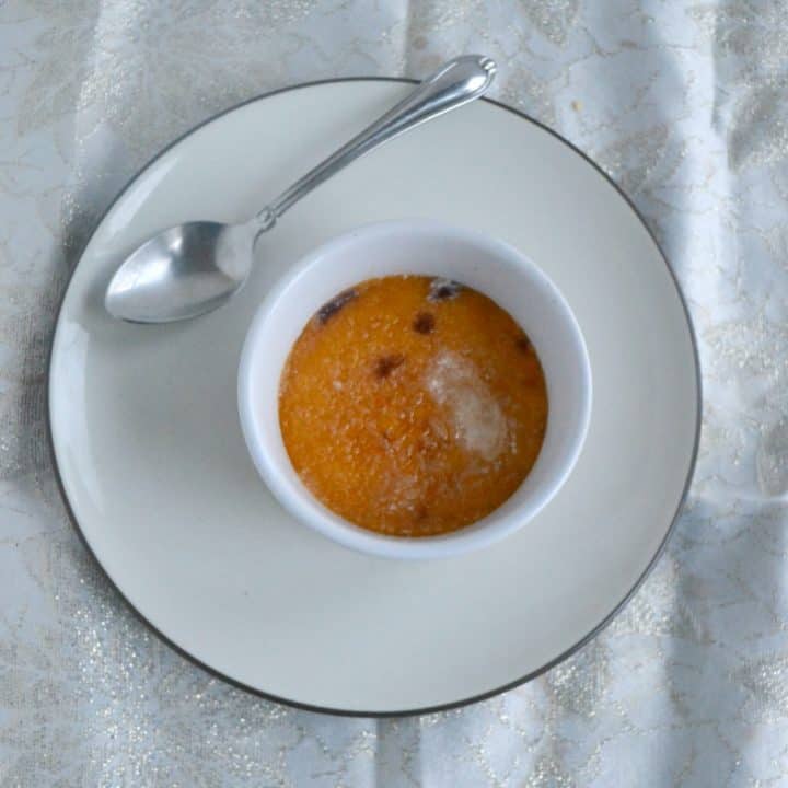 A ramekin filled with persimmon and cranberry creme brulee with a sugar glass top and a spoon sitting on the plate behind the ramekin.