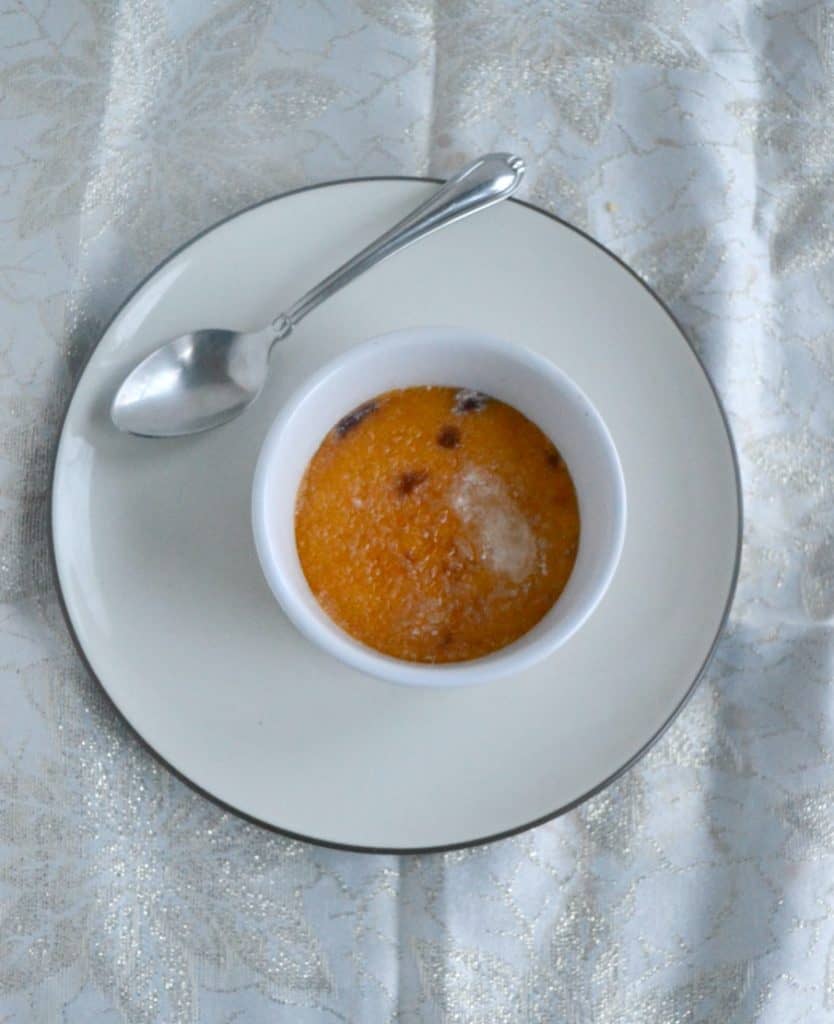 A ramekin filled with persimmon and cranberry creme brulee with a sugar glass top and a spoon sitting on the plate behind the ramekin. 