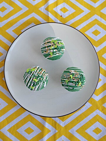 A plate with three green Hot Chocolate Bombs on it on a yellow background.