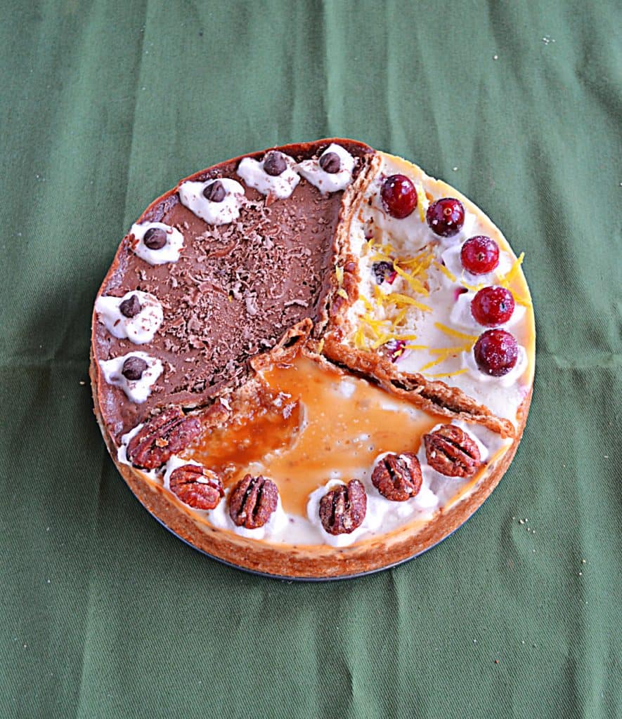 A cheesecake divided into 3 sections: One is orange cranberry with whole cranberries on top, one third is caramel pecan cheesecake topped with caramel and pecan halves, and one third is chocolate espresso topped with espresso beans.